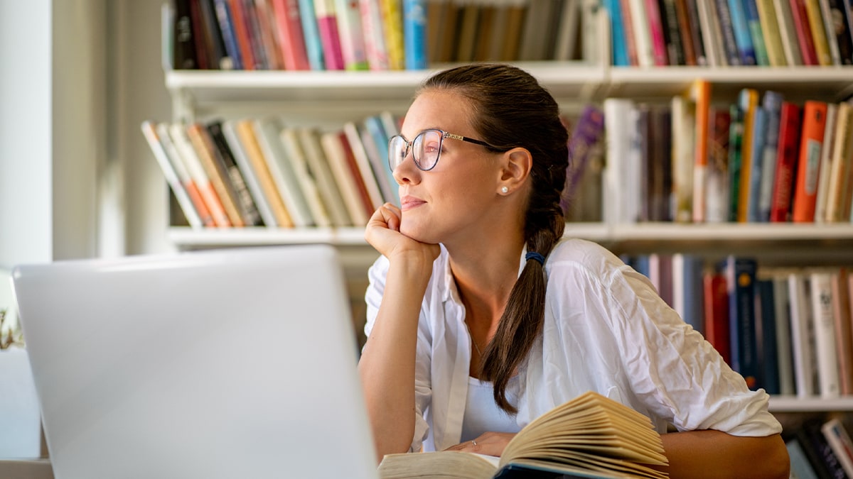 Young woman seated at desk in home office with laptop starring outside.