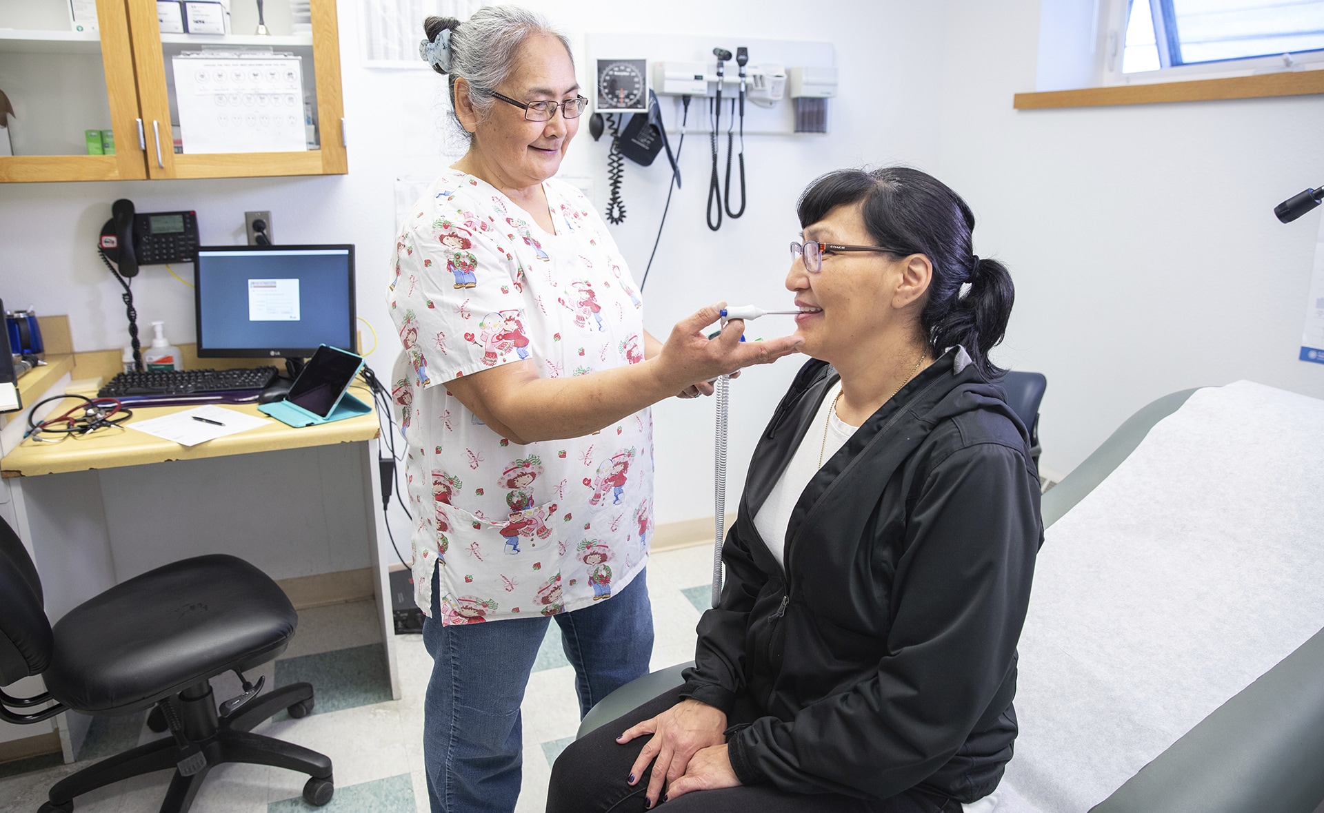 Woman in a doctor's office getting her temperature taken by medical worker.