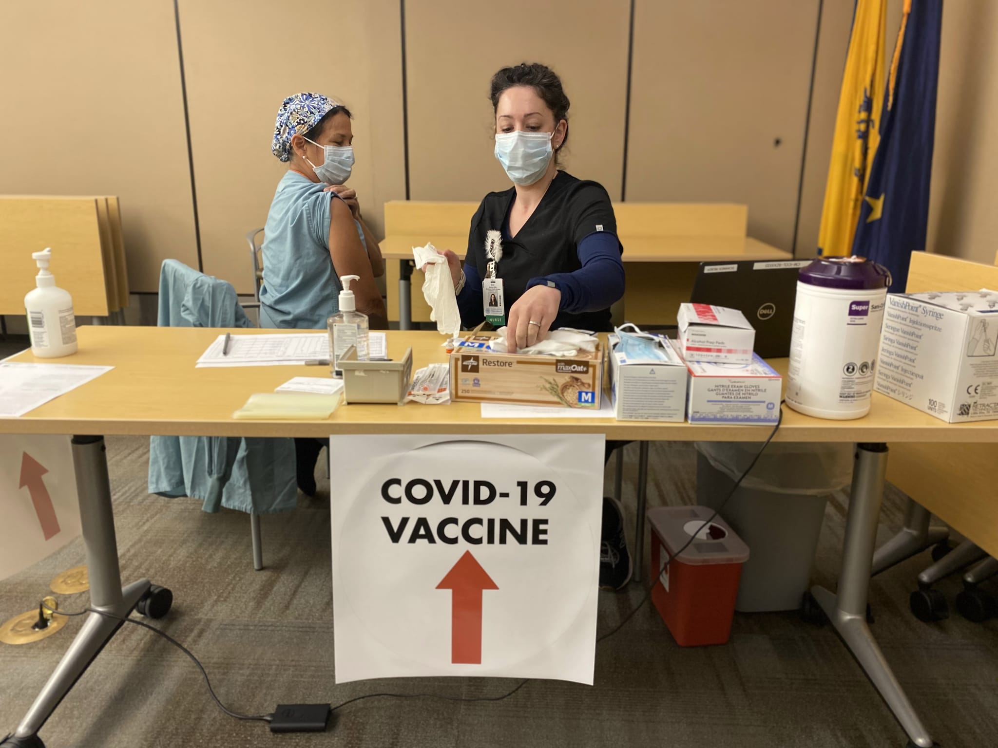 Health care worker prepares COVID-19 vaccine for female patient sitting in a chair.