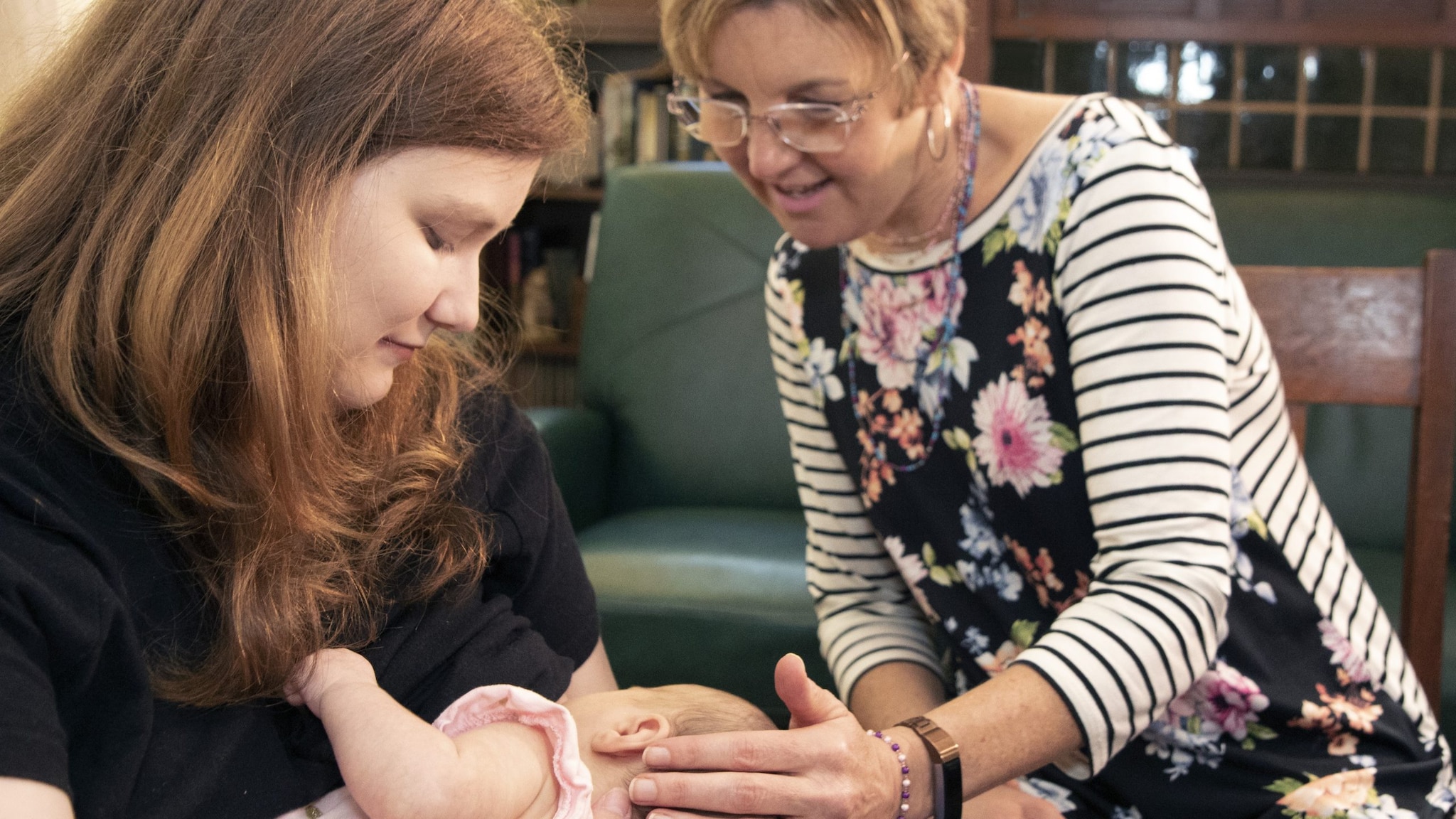 A mother breastfeeds her infant with support from an older woman.