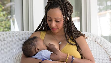 Woman breastfeeding while sitting in a wicker seat.