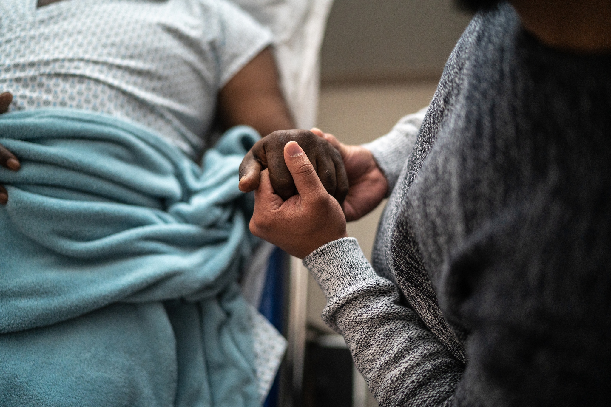 A hospitalized patient holding the hand of a loved one