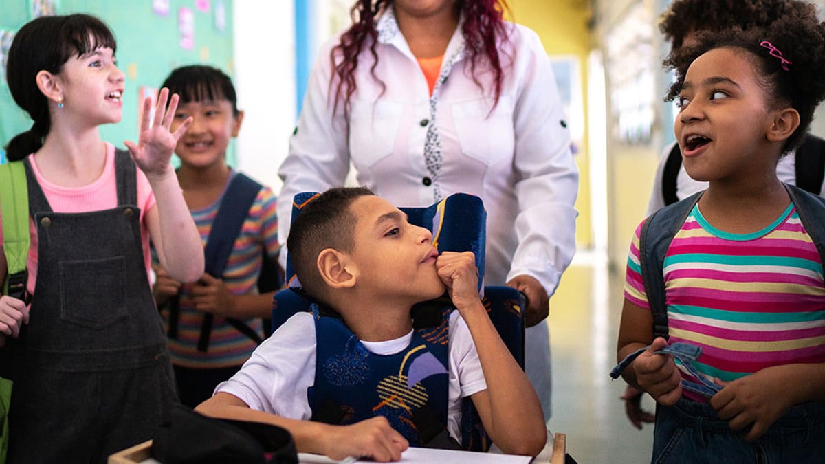 Teacher and students walking in the corridor at school, including a student with a disability