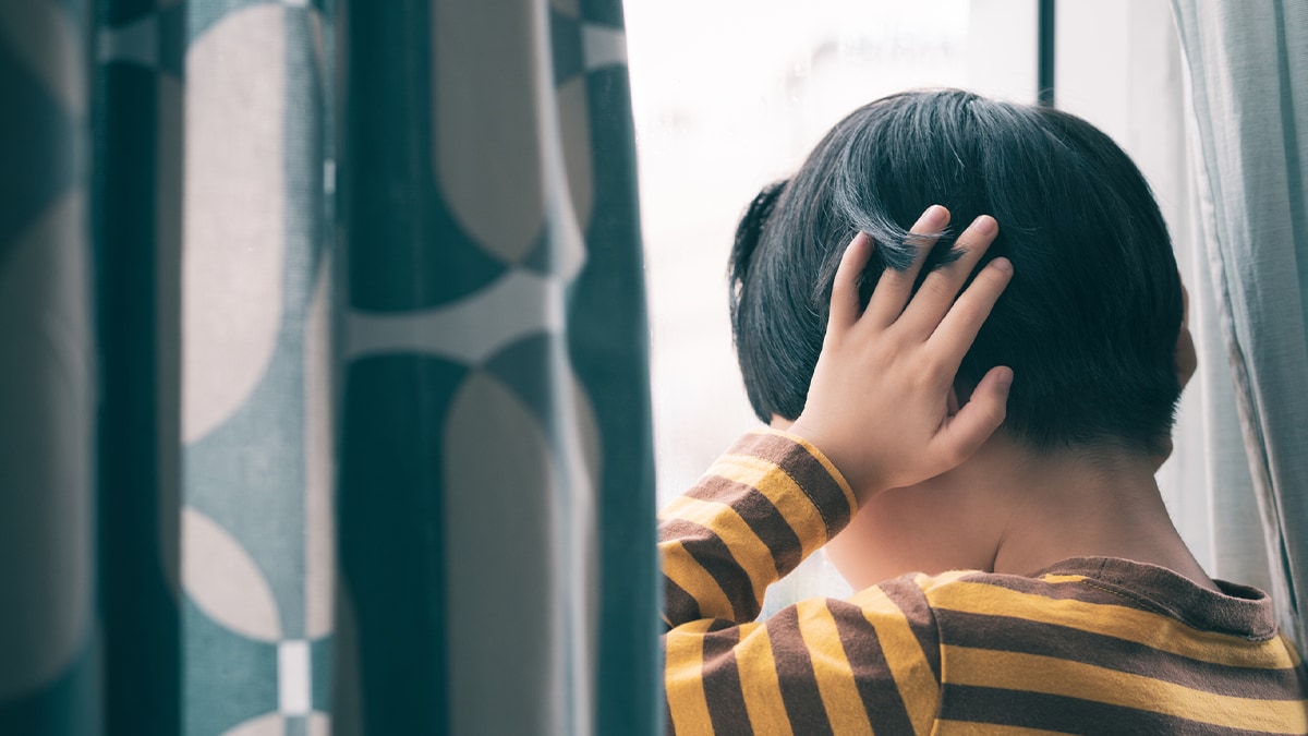 child holding ears next to window