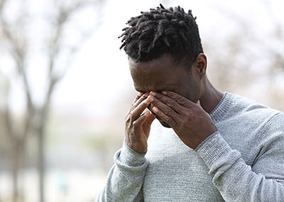 Man stands outside rubbing his eyes because of pink eye.