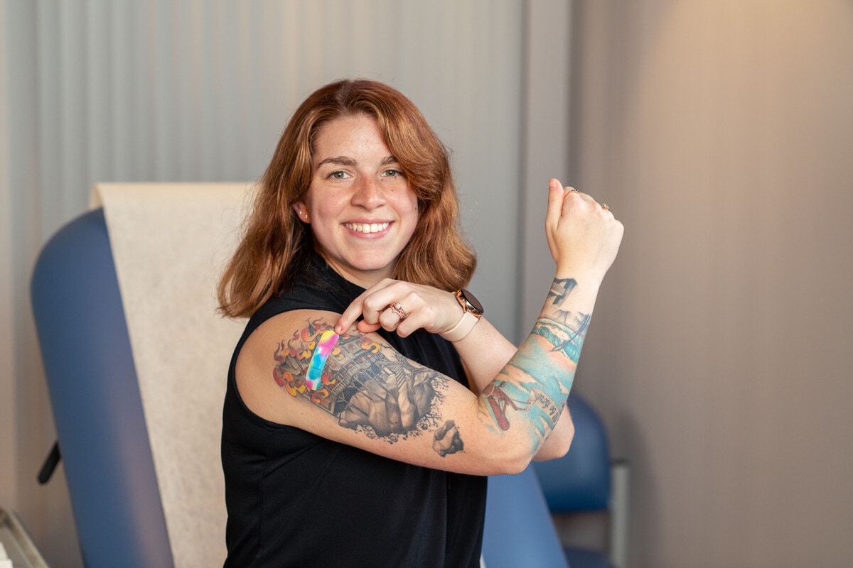 Young woman showing off her recent COVID vaccine and Band-Aid on tattooed upper arm.