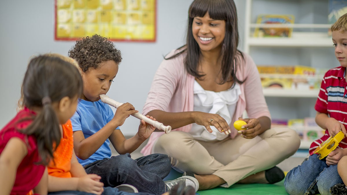 Teacher sitting in a circle with elementary age children playing the recorder.