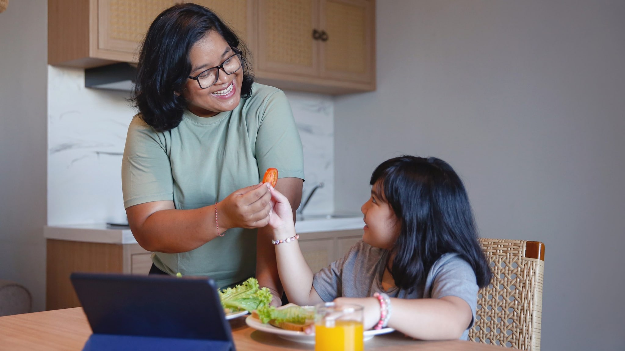 Mother giving daughter a slice of tomatoes for a sandwich.