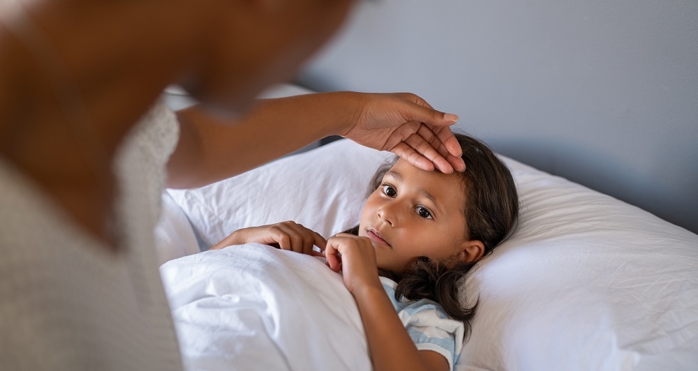 Parent uses hand to check temperature of child sick in bed.