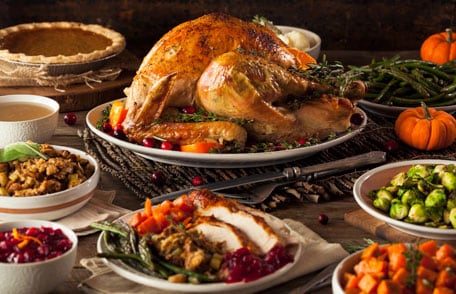 Whole, roasted turkey on table with traditional Thanksgiving sides around it.