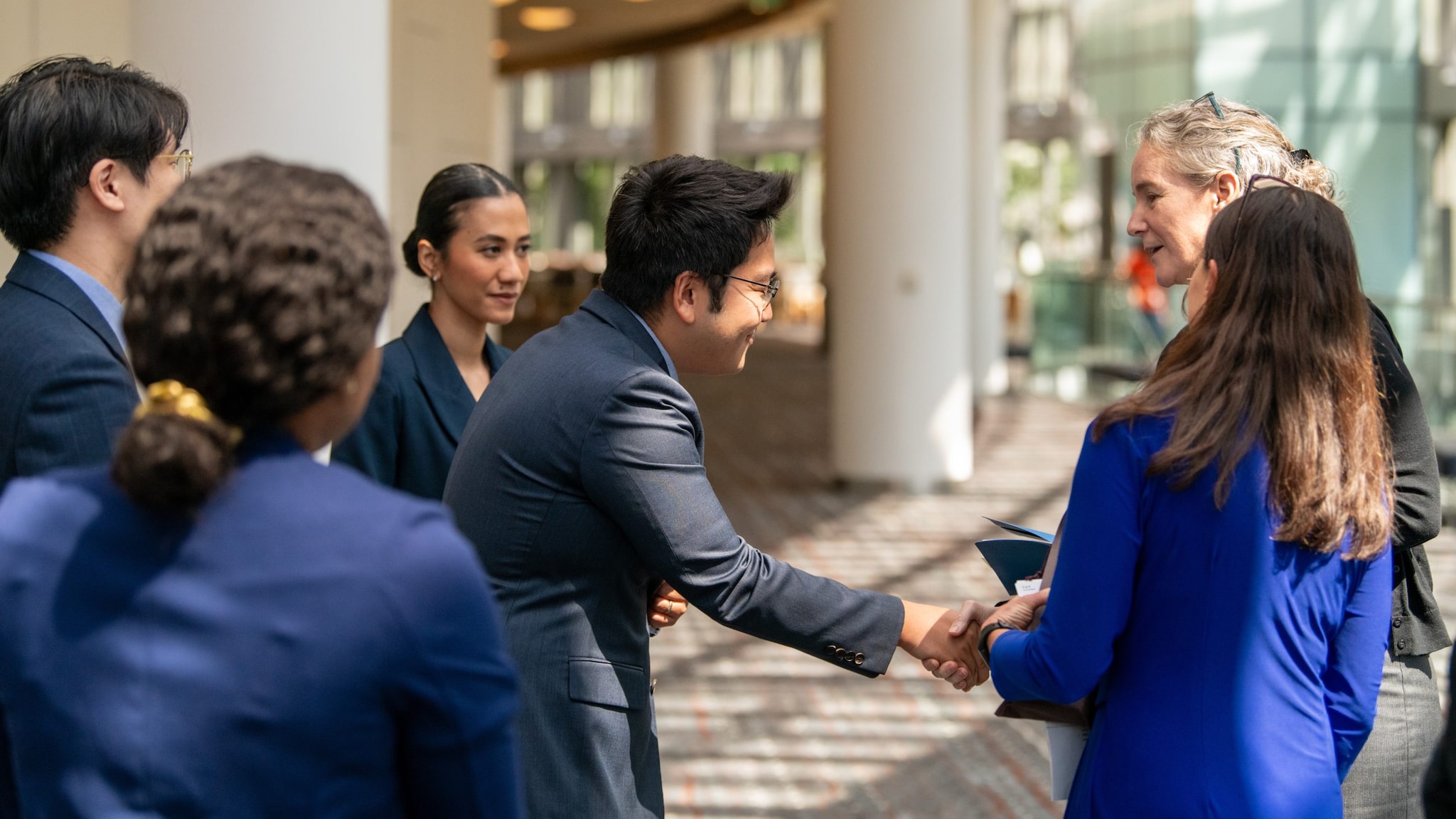 A group of men and women of all ethnicities standing in a group while two members shake hands