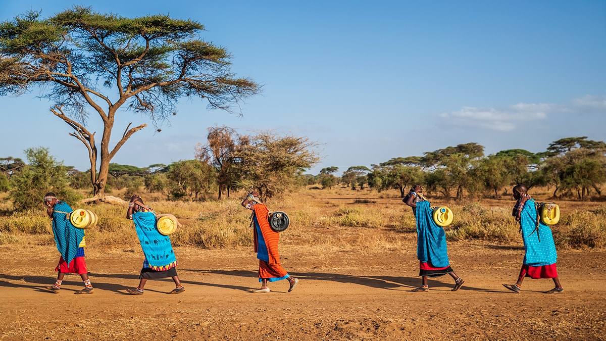 Global Health Observances - people wearing colorful patterned clothing walk barefoot across a dirt road.