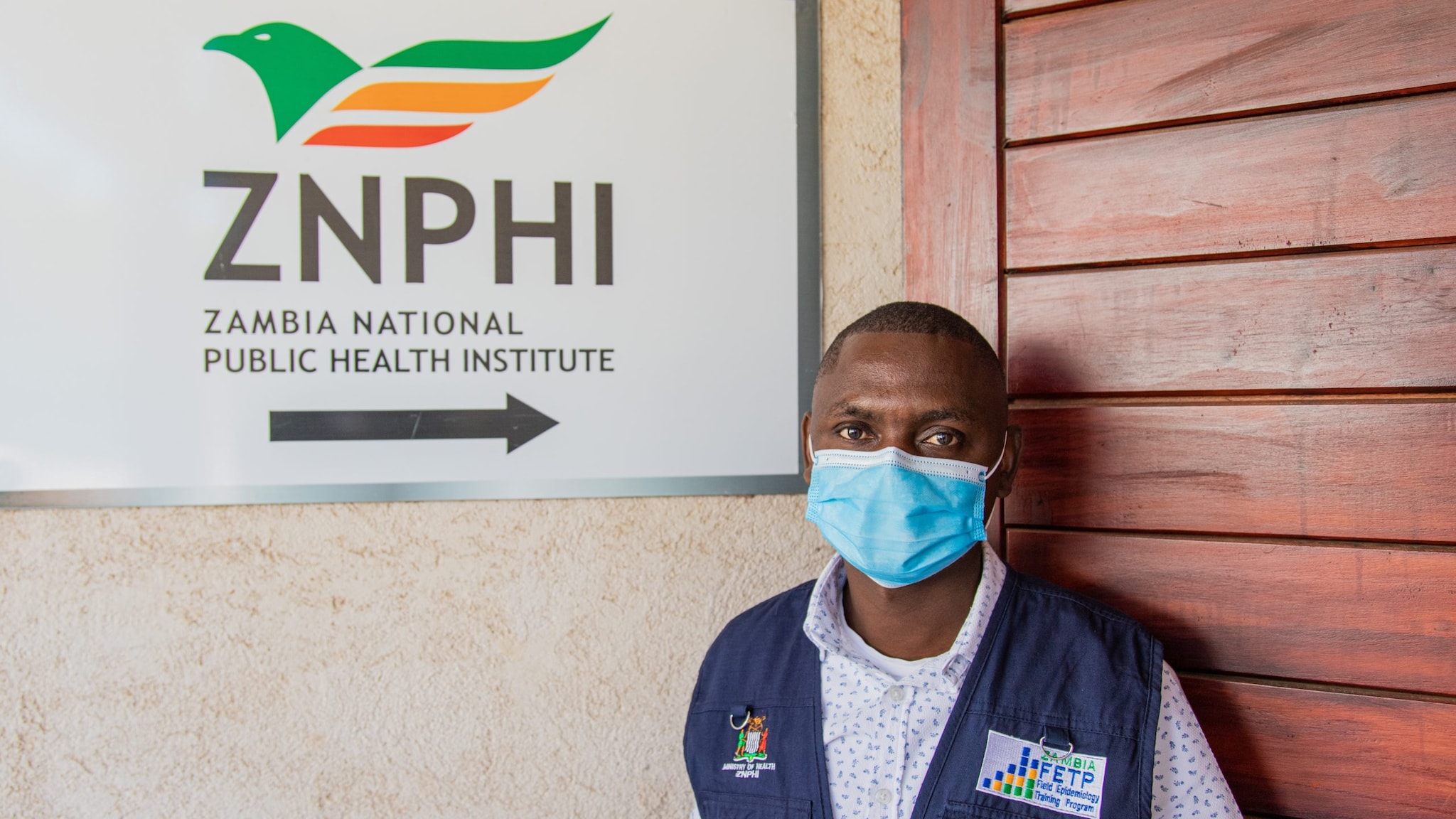 Dr. Dabwitso Banda stands outside of the Zambia National Public Health Institute with Mask on.