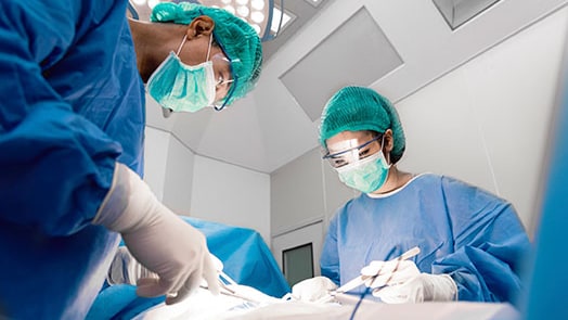 Doctors and nurse with tools in hands performing surgery in operation room.