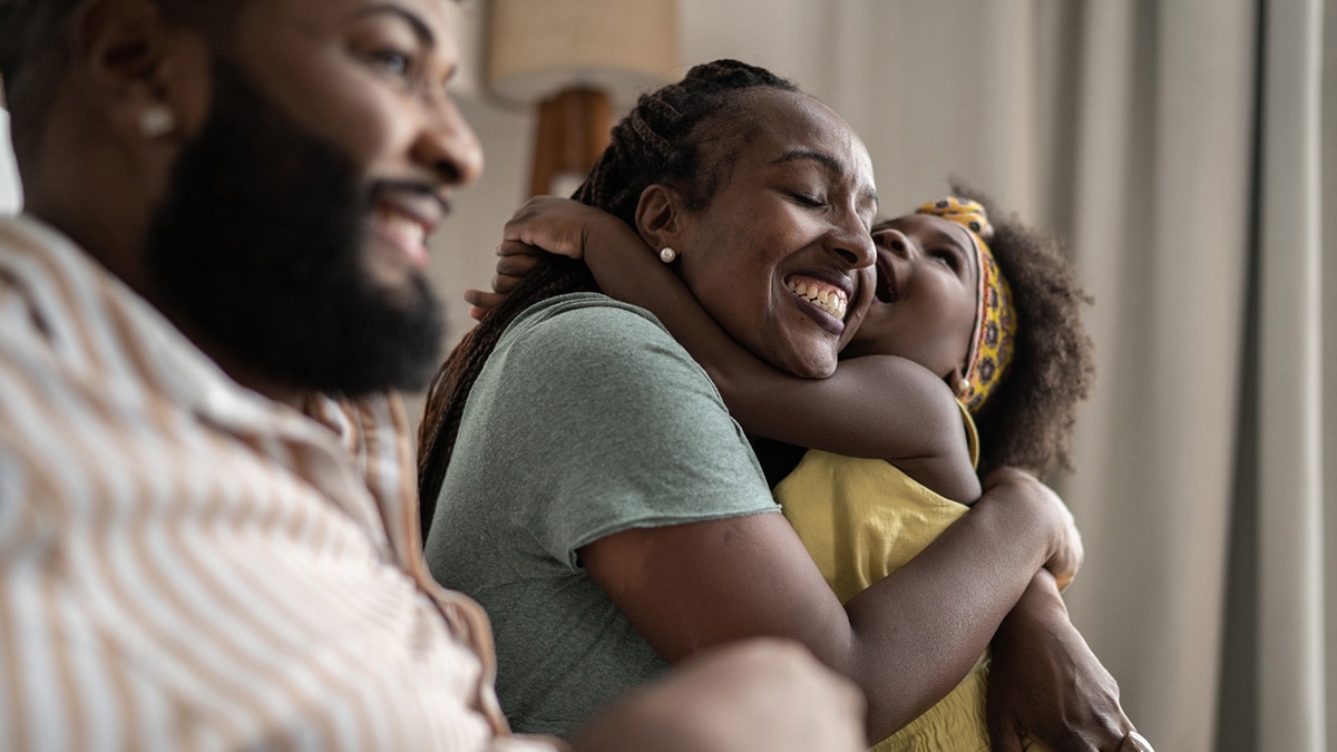 A man, woman, and child share hugs and laughs.