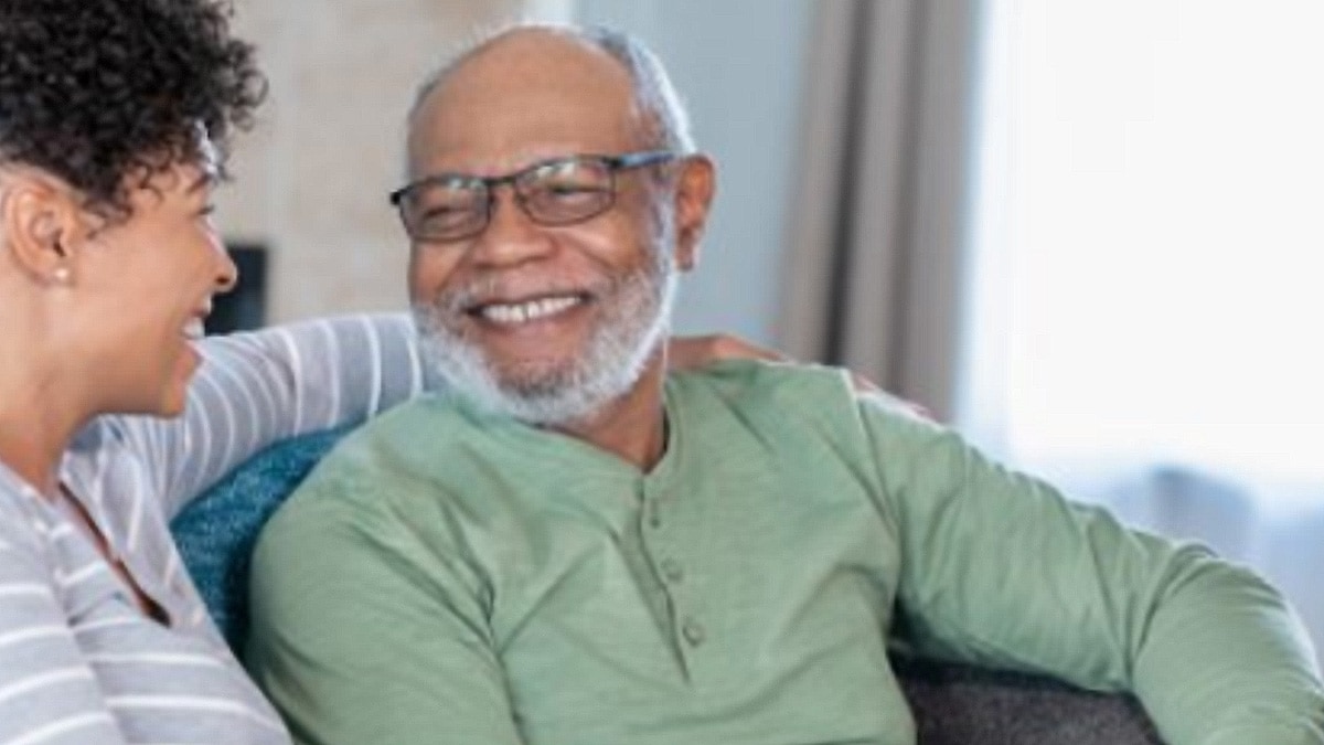 Older man and woman sitting together on a sofa, smiling at each other.