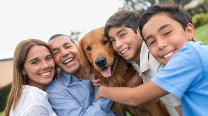 A family of mom, dad, and two sons hugging a dog