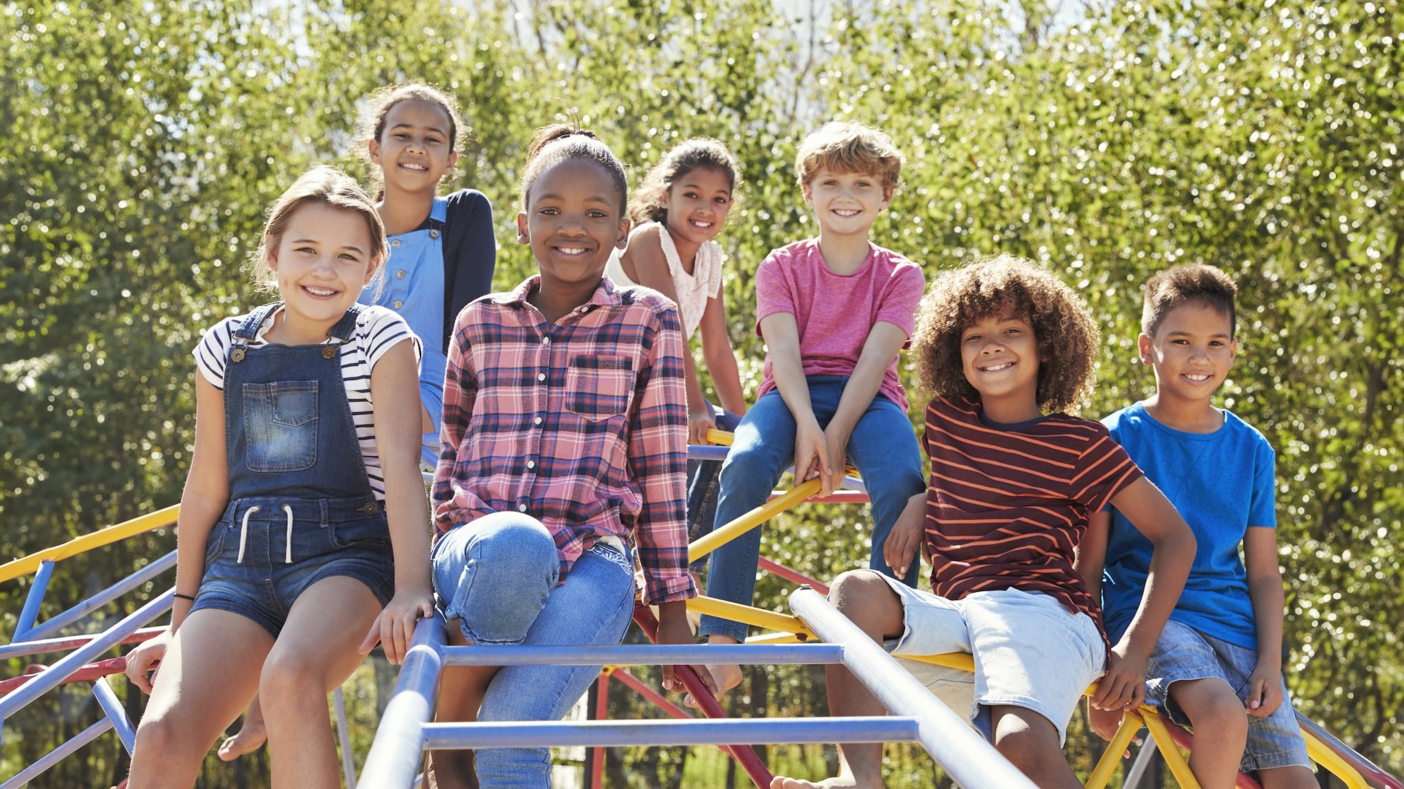 A group of pre-teens siting on a playground climbing frame, smiling.