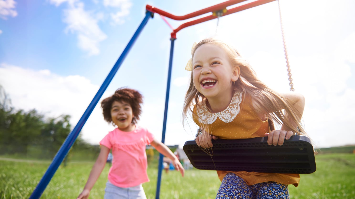 Child on a swing with another child approaching the swings.