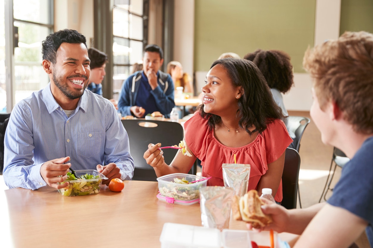 Teachers and students eating lunch together in a school cafeteria.