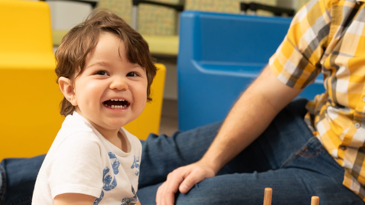 child sitting on ground smiling next to his dad