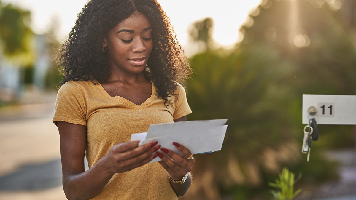 A woman standing in front of her mailbox checking her mail