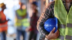 Man holding a hard hat and wearing a high visibility vest.