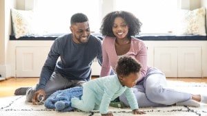 Smiling parents sitting on floor with crawling baby.