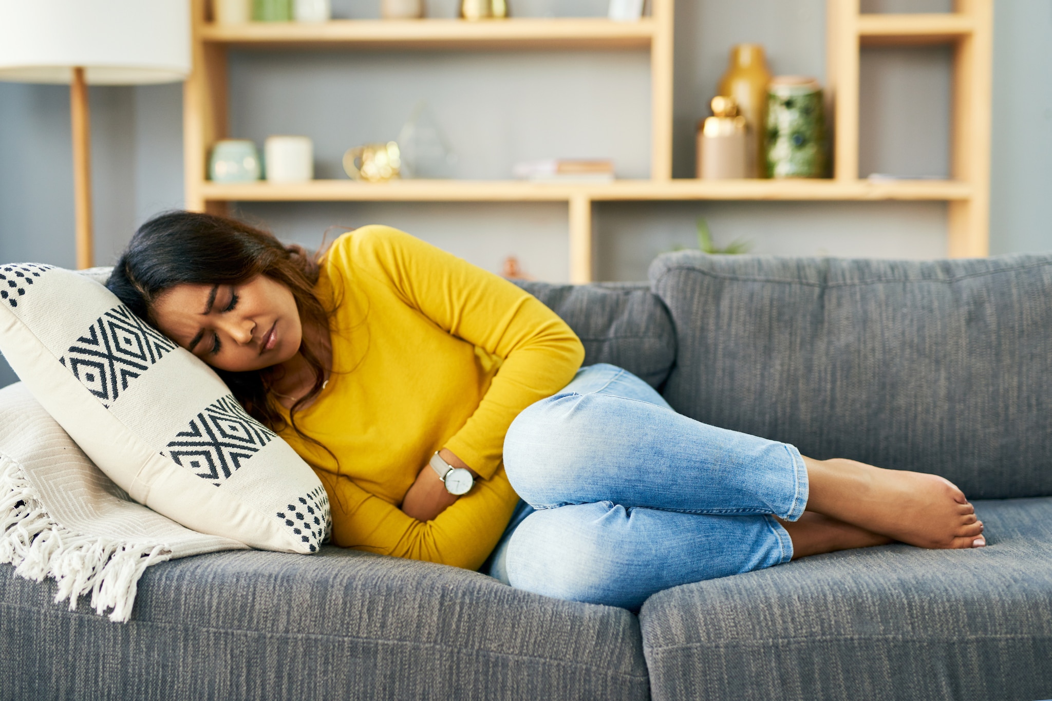 Young woman laying down on couch in abdominal pain.