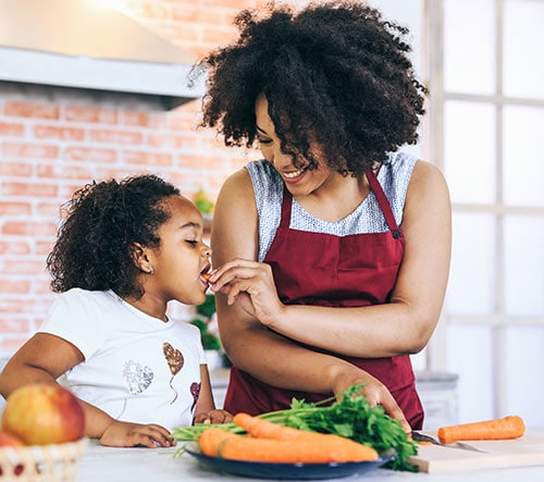 A mother feeding a carrot to her child