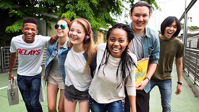 Diverse group of teenagers outside, smiling and walking forward with their arms around each other.