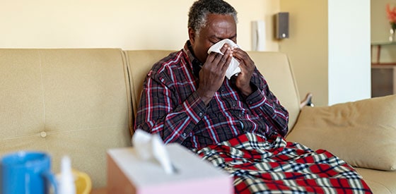 Man sitting on couch blowing his nose