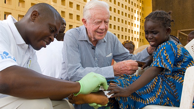 President Carter comforts a young girl as she receives medical care for Guinea worm disease.