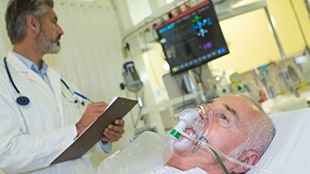 Patient in hospital bed, with doctor charting at the bedside