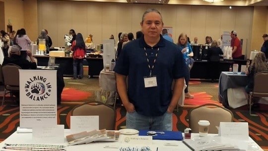 Photo of Abraham Bearpaw standing at a health fair table.