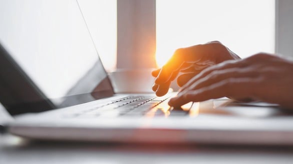 A person typing on a laptop with a sunrise in the background.