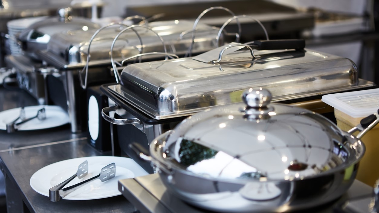 Several large covered food serving pans with heated burners underneath.