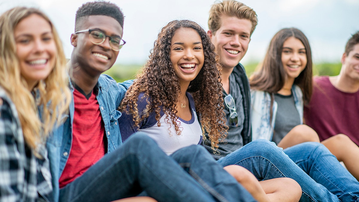 Diverse group of young adults sitting in a line and embracing outside.