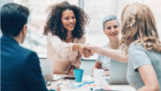 A group of people where two women are shaking hands.