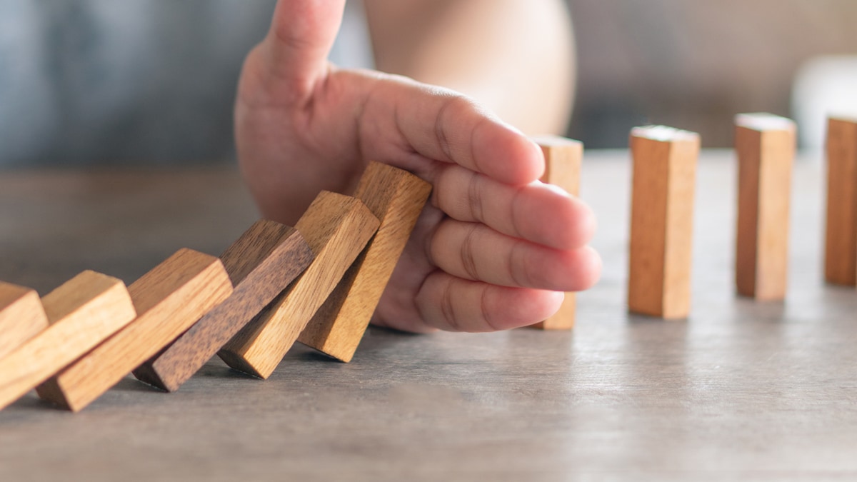 a hand blocking the falling of tiles to prevent others from falling - metaphor for prevention