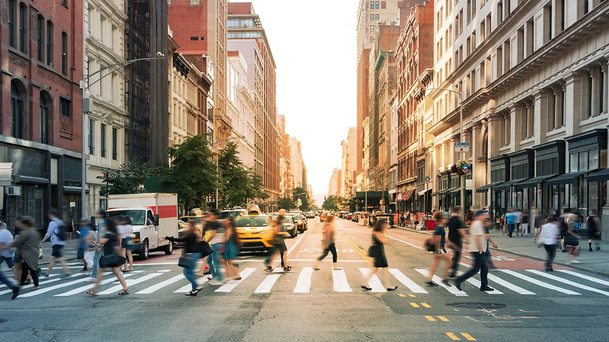 Crowds of people walking through a busy crosswalk at an intersection in Midtown Manhattan, New York City