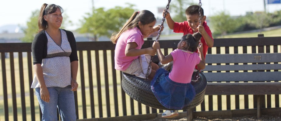 a mother watching her three children play on a tire swing