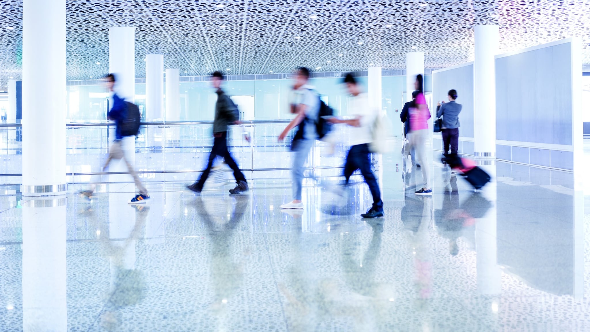 A group of people walking through an airport to a flight, carrying luggage.