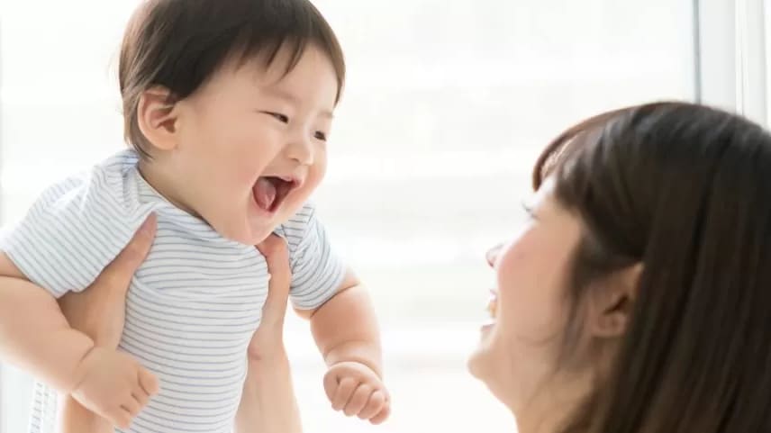 A mother holding up and smiling at her young baby.