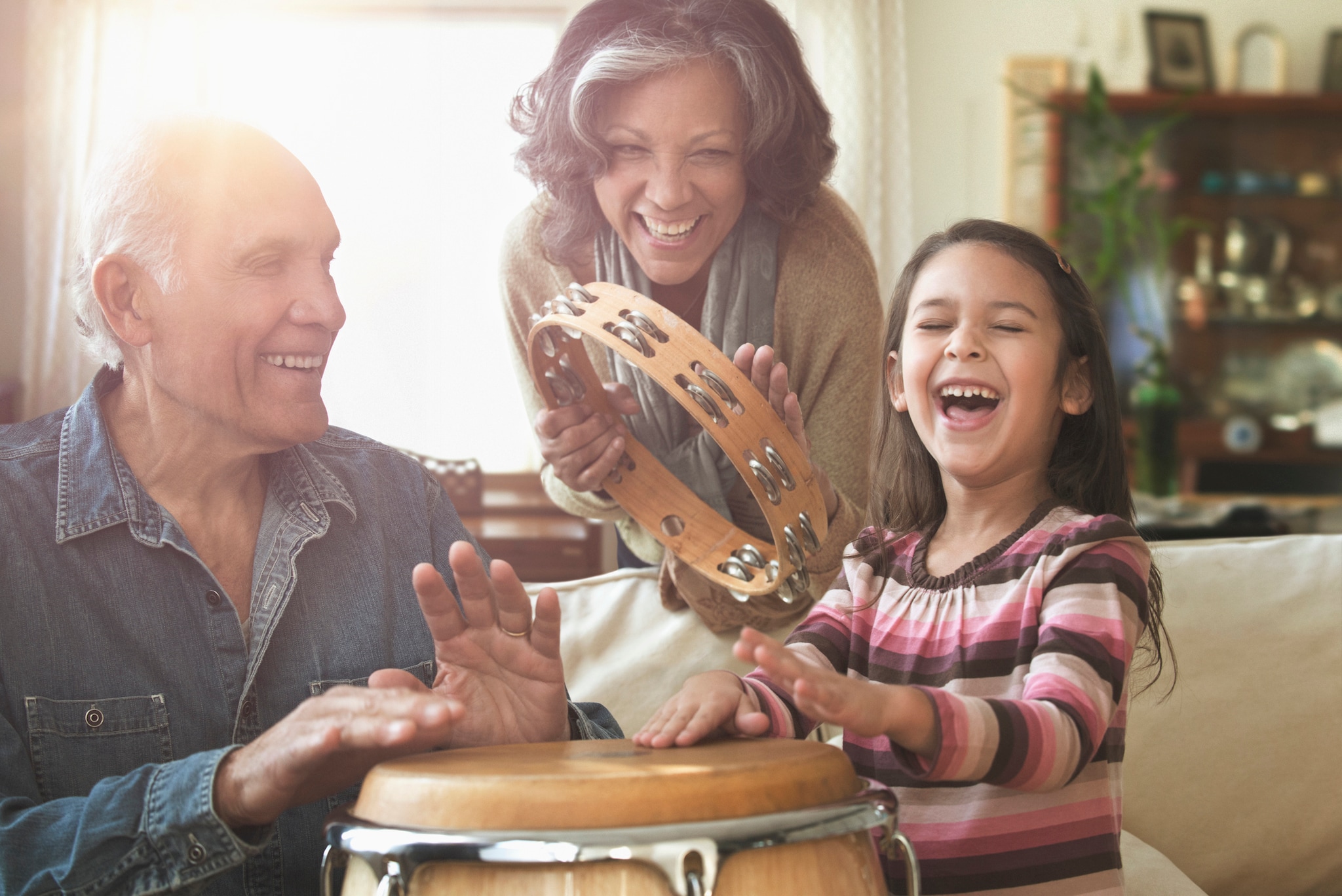 Grandparents and grandchild laughing and playing musical instruments together at home.