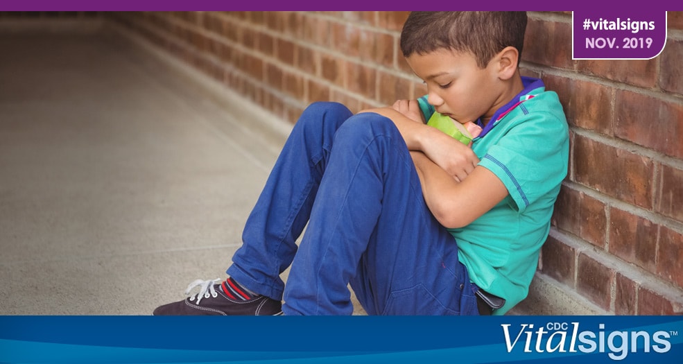 A child hugging a toy to his chest while sulking against a brick wall.