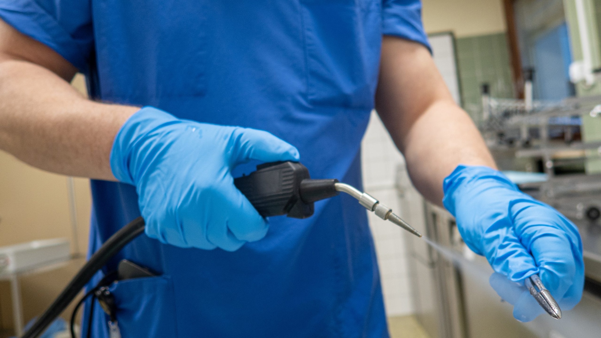 A doctor's hands wearing blue sterile gloves while sanitizing a medical instrument with pressurized water.